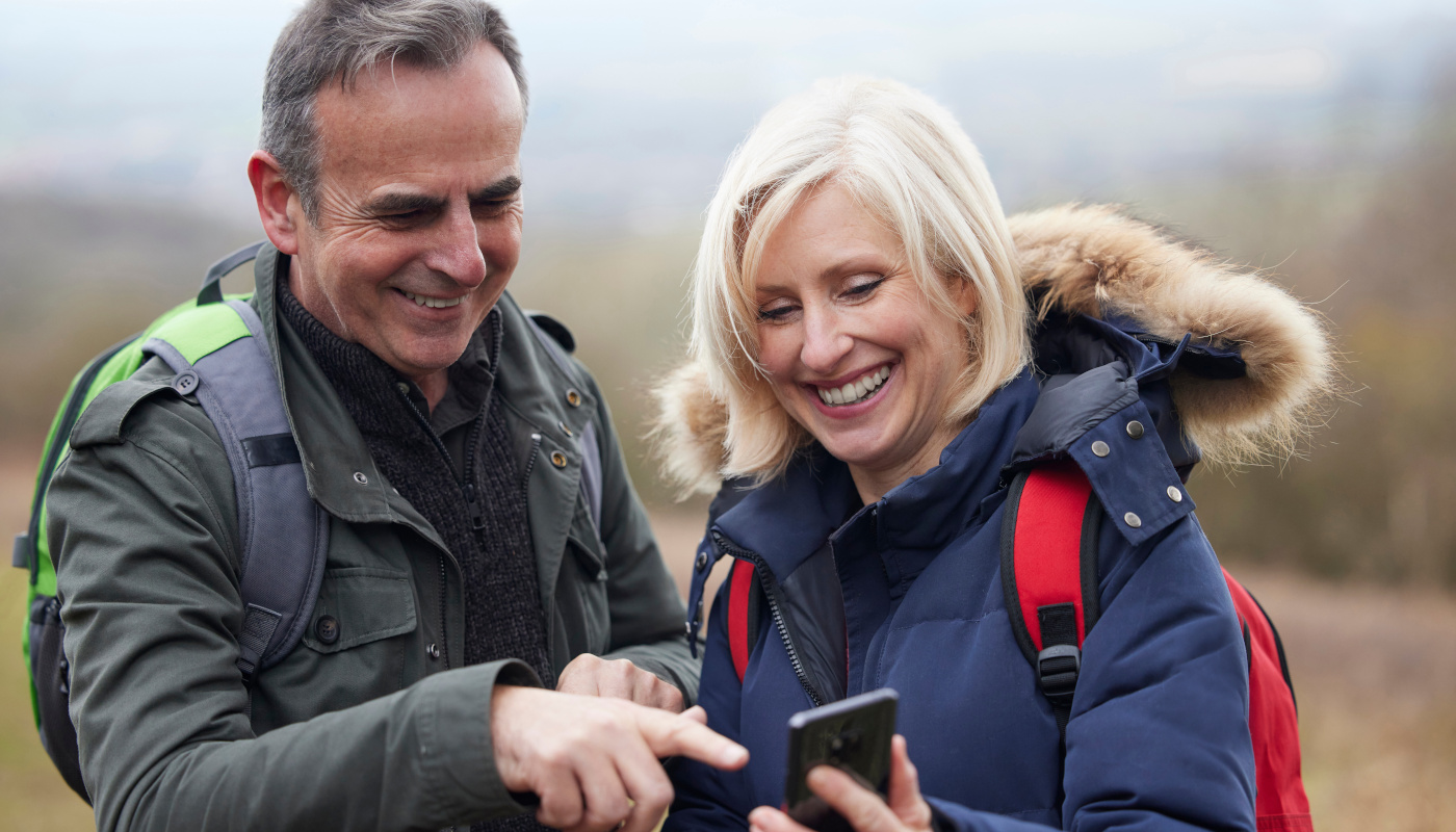 Älteres Ehepaar beim Wandern schaut lächelnd gemeinsam auf das Handy der Frau